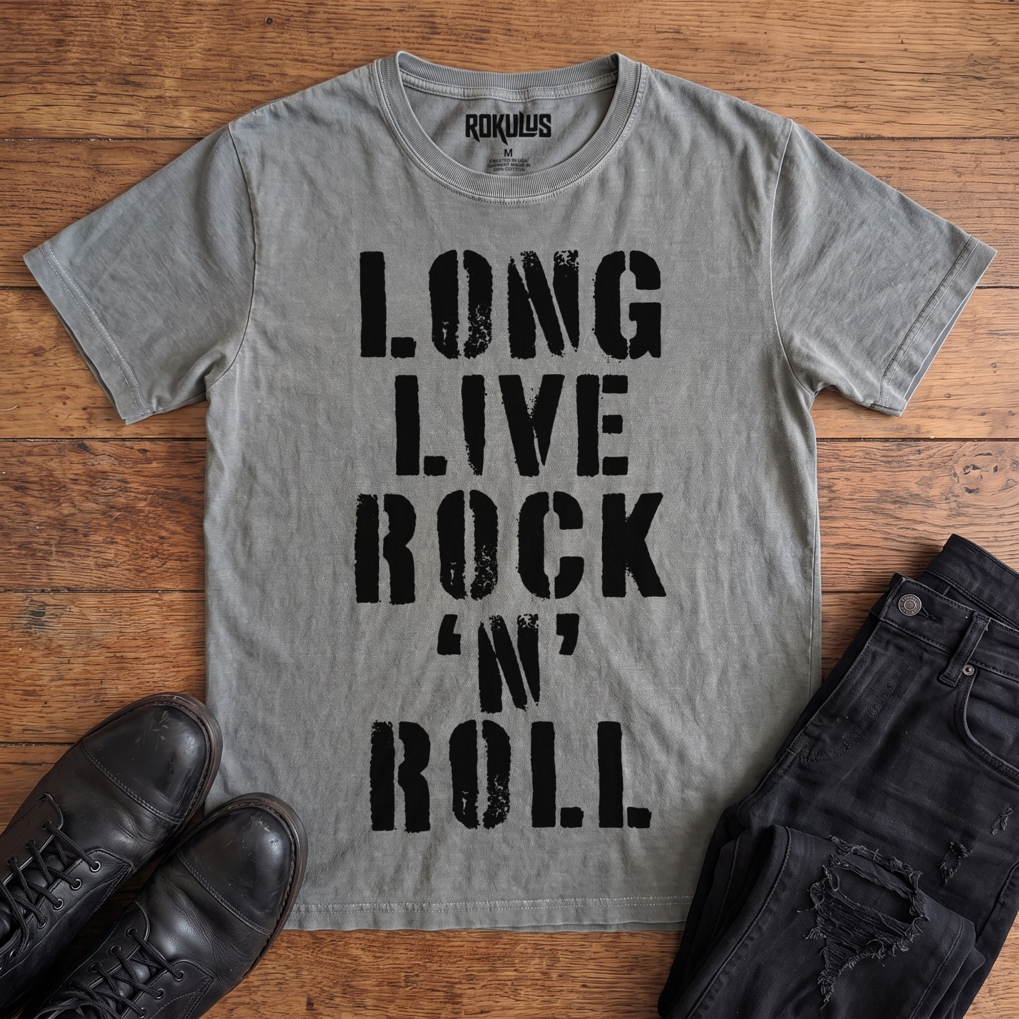 Washed grey Rokulus Long Live Rock 'n' Roll vintage graphic tee laid flat on wood with black boots and jeans, front print showing "Long Live Rock 'n' Roll" stacked vertically in heavy distressed black stencil lettering