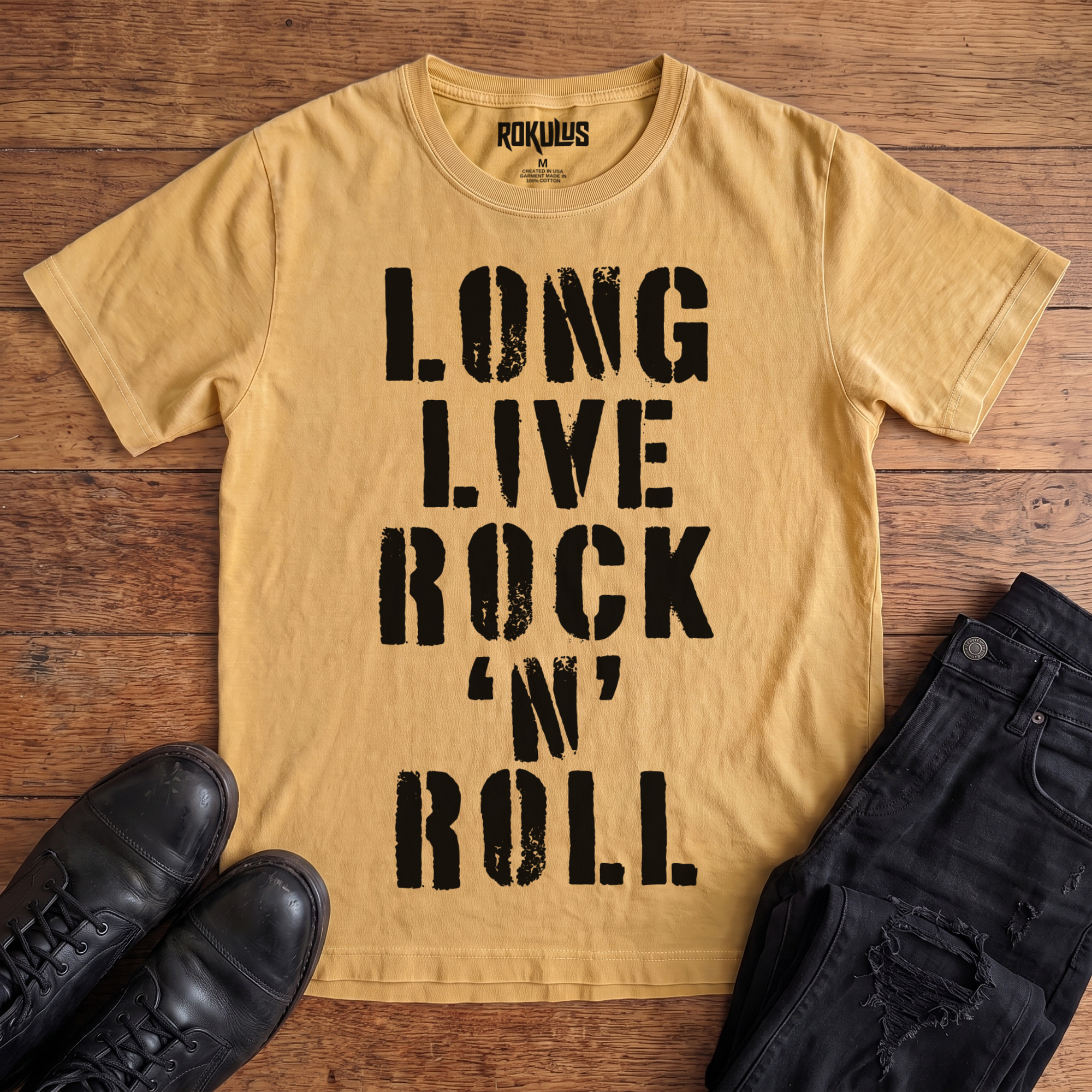 Washed mustard Rokulus Long Live Rock 'n' Roll vintage graphic tee laid flat on wood with black boots and jeans, front print showing "Long Live Rock 'n' Roll" stacked vertically in heavy distressed black stencil lettering