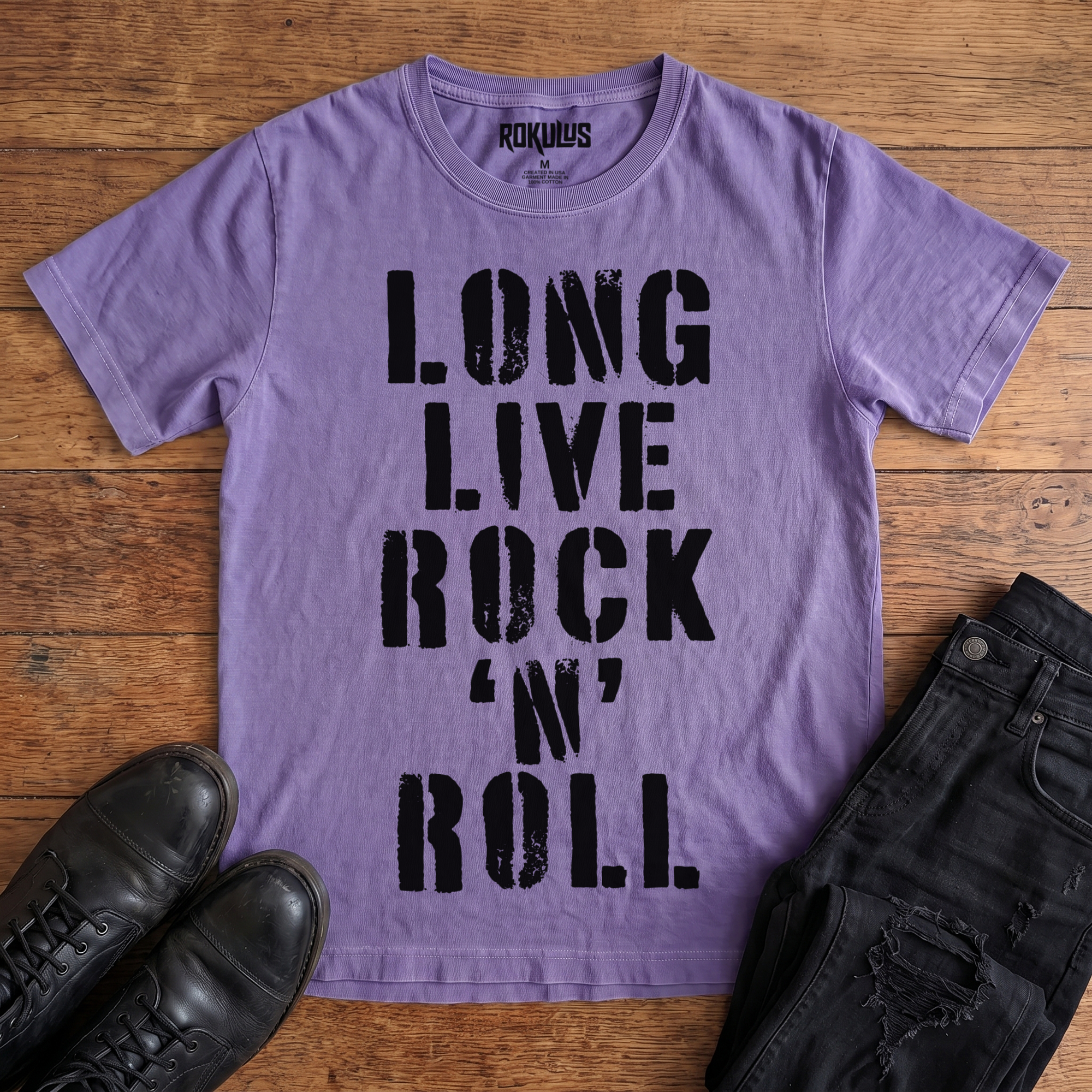 Washed purple Rokulus Long Live Rock 'n' Roll vintage graphic tee laid flat on wood with black boots and jeans, front print showing "Long Live Rock 'n' Roll" stacked vertically in heavy distressed black stencil lettering