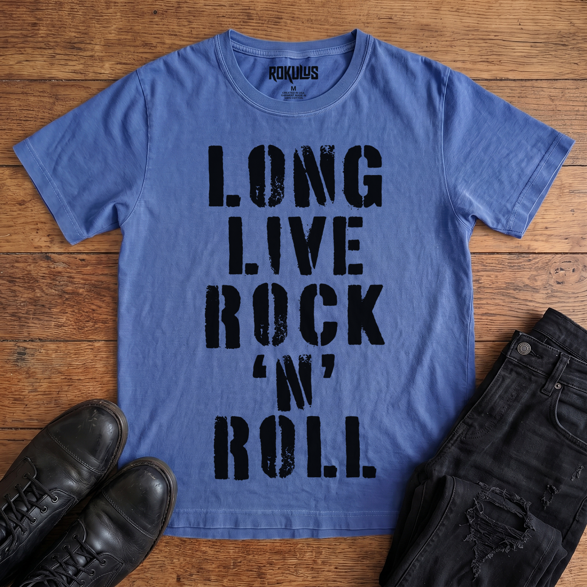 Washed royal blue Rokulus Long Live Rock 'n' Roll vintage graphic tee laid flat on wood with black boots and jeans, front print showing "Long Live Rock 'n' Roll" stacked vertically in heavy distressed black stencil lettering