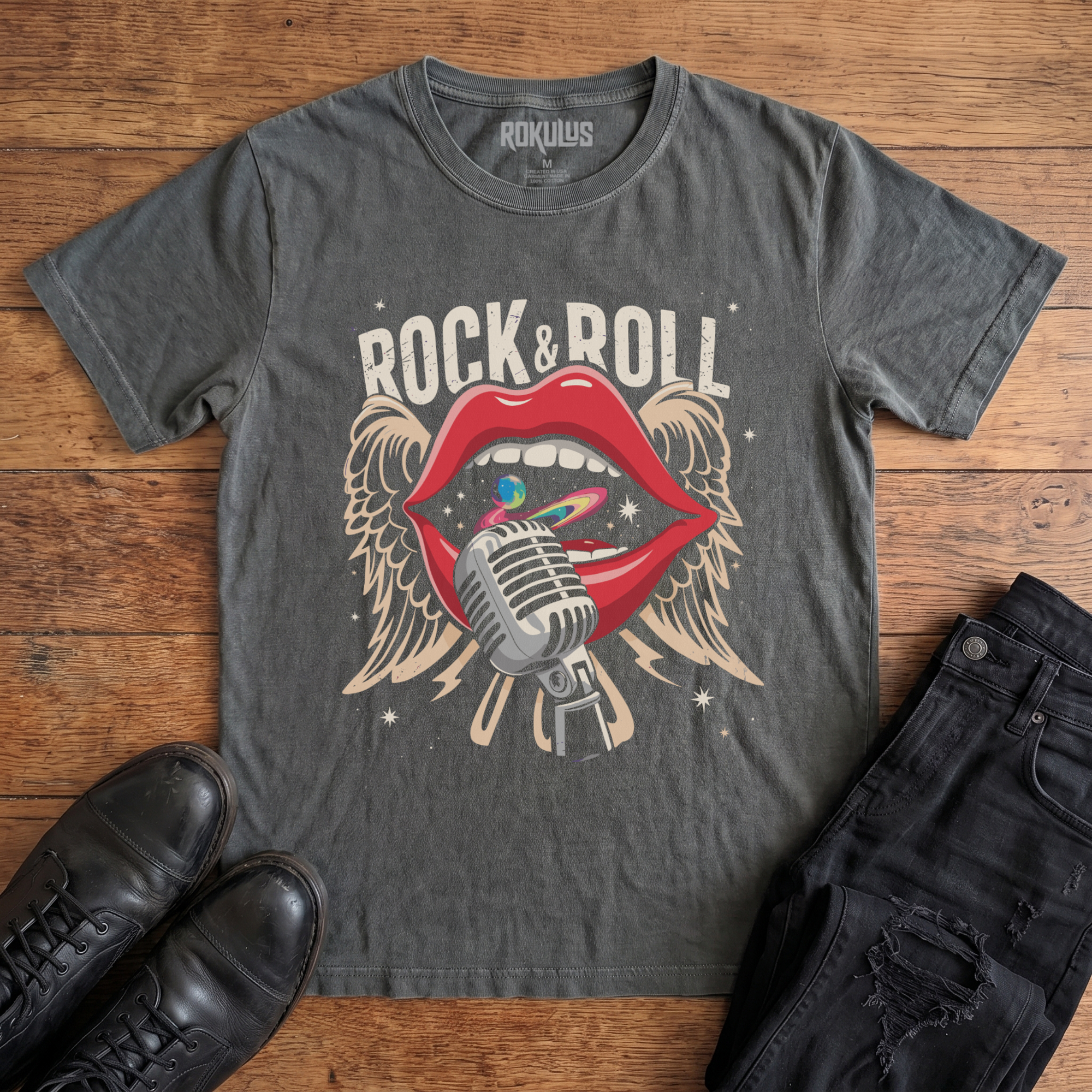 Washed Charcoal Rokulus Rock & Roll Lips vintage graphic tee laid flat on wood with black boots and jeans, front print showing bright red lips around a chrome microphone with cosmic swirl and cream angel wings under arched "Rock & Roll" lettering