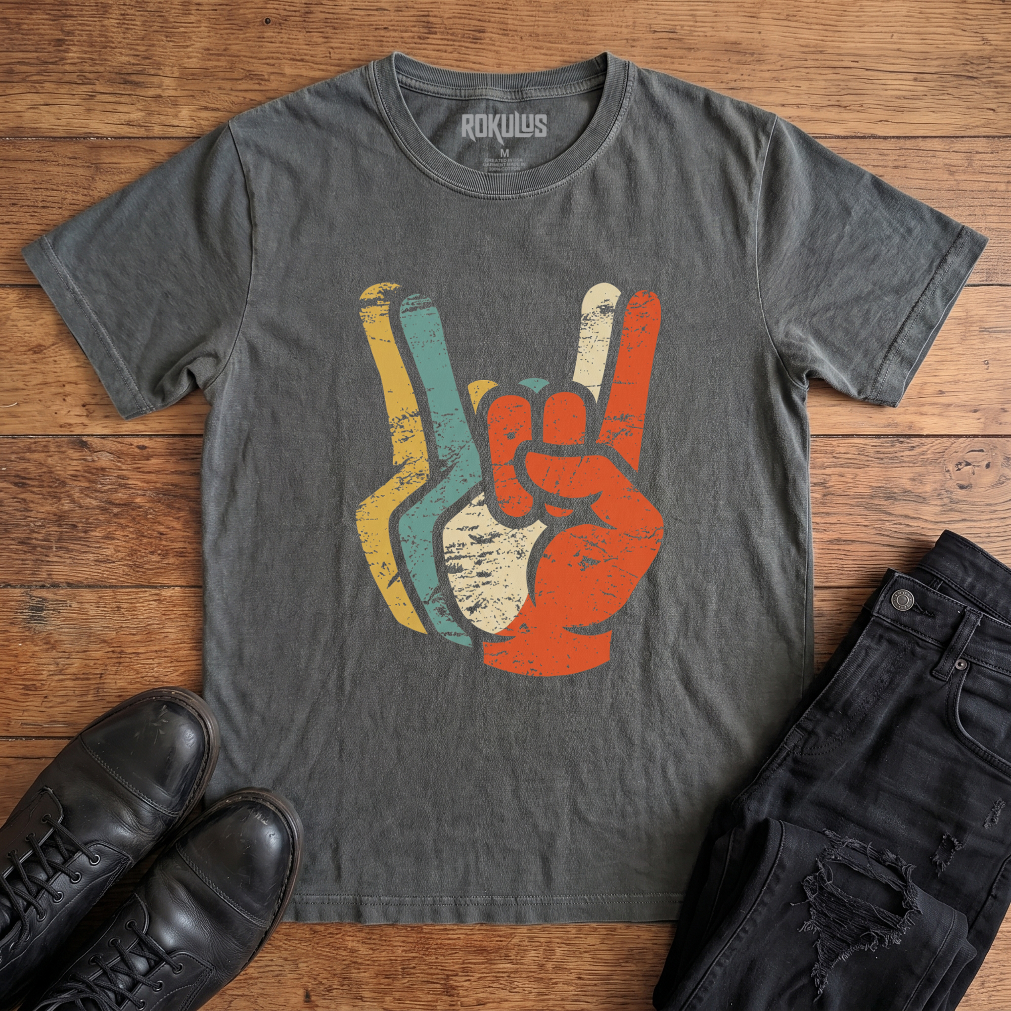 Washed charcoal Rokulus Retro Rocker Hands vintage graphic tee laid flat on wood with black boots and jeans, front print showing a devil-horns rock salute layered in distressed retro mustard, teal, cream, and burnt orange tones