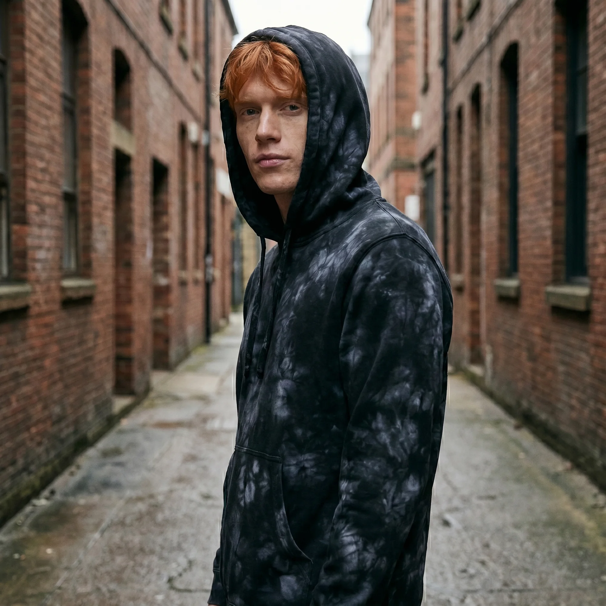 Man wearing an black tie-dye hoodie with the hood up, side view