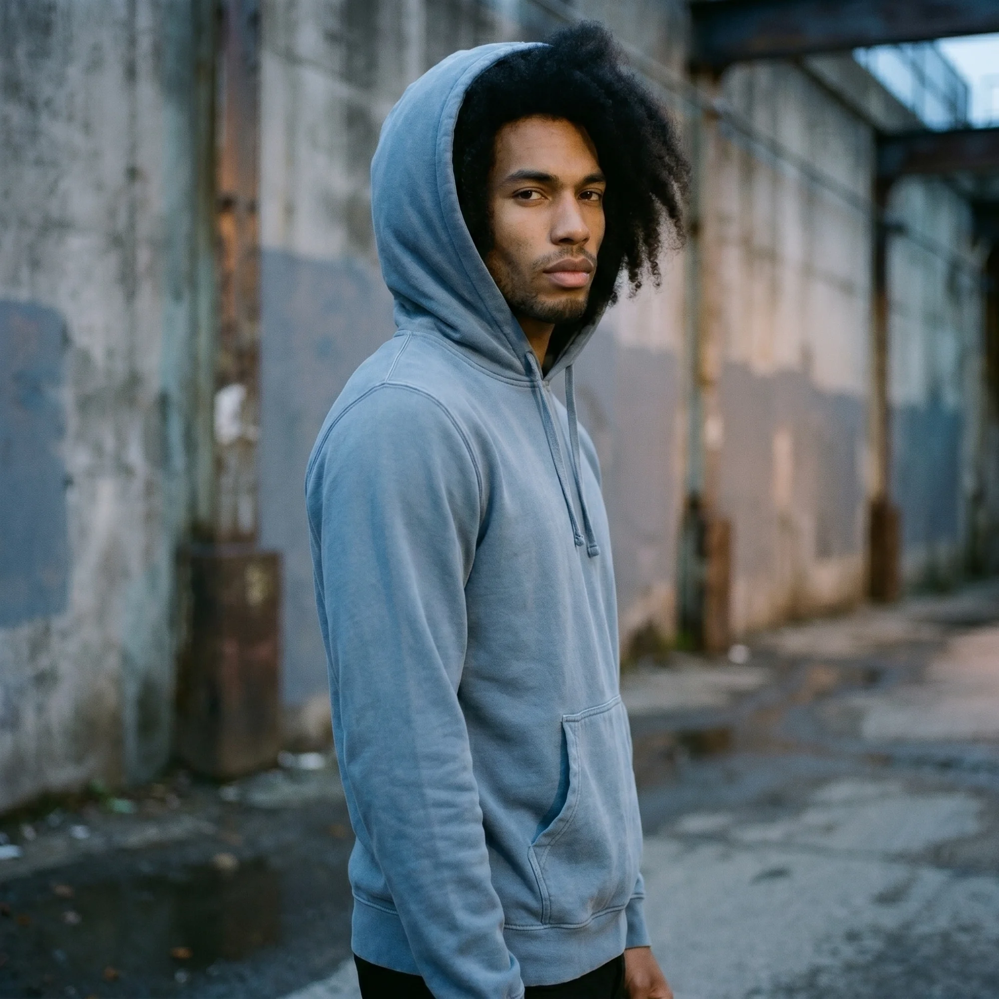 Man wearing a slate blue pigment dye hoodie with the hood up, side view