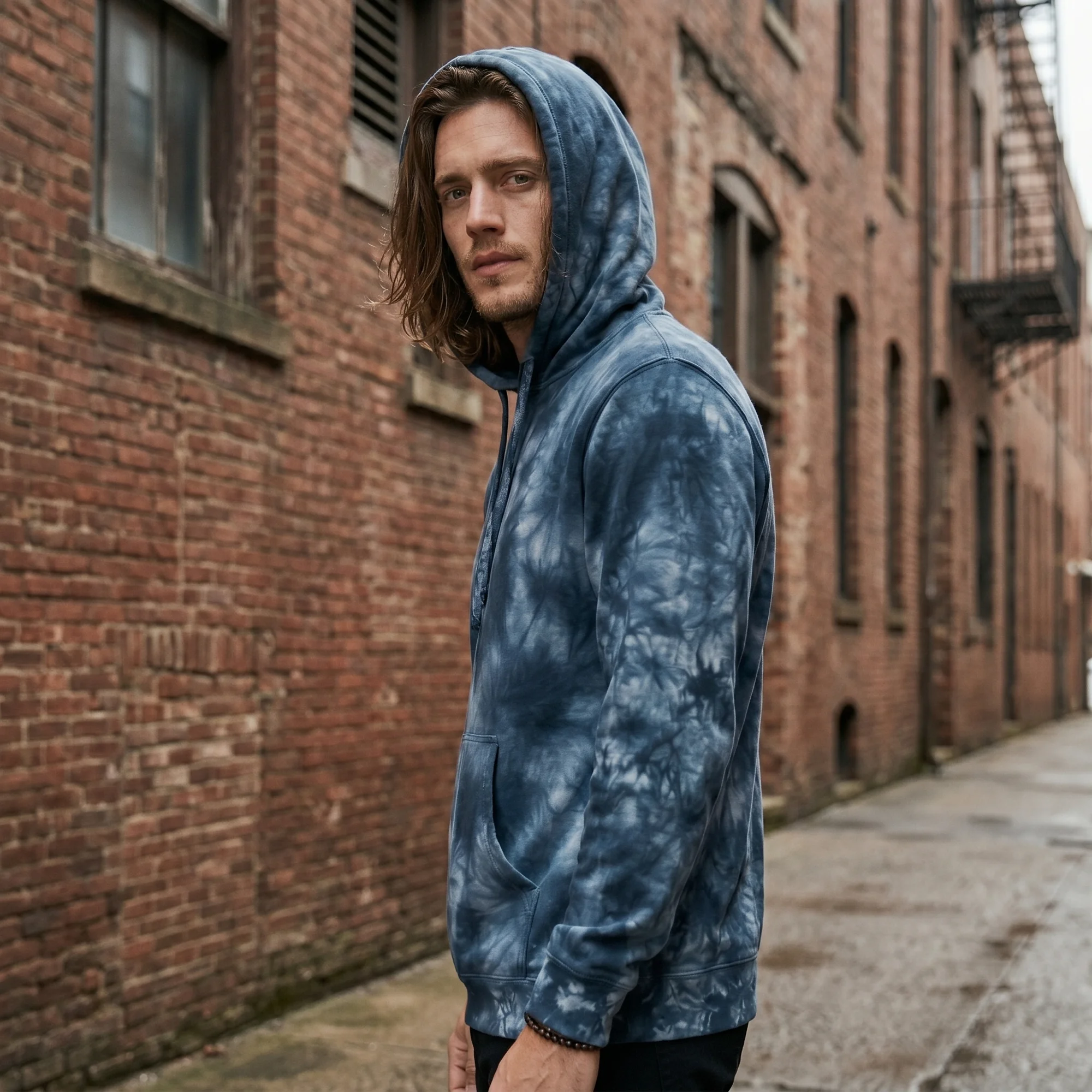 Man wearing an navy tie-dye hoodie with the hood up, side view