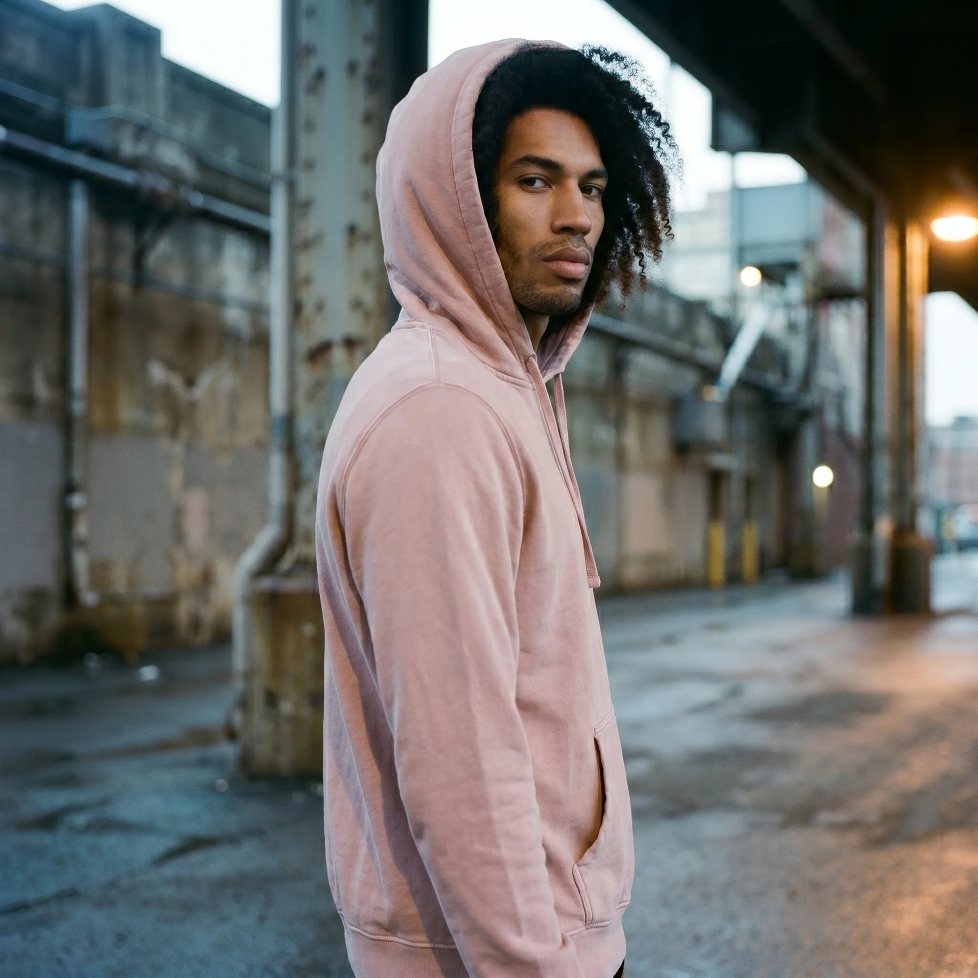 Man wearing a pink pigment dye hoodie with the hood up, side view