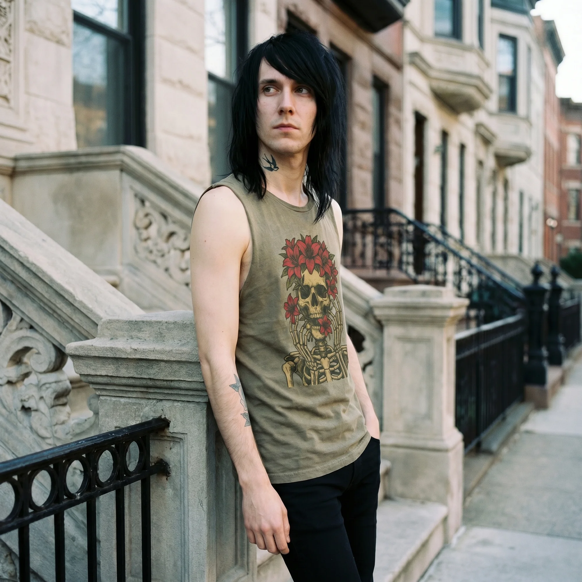 Man with long black hair leaning against a stone stoop railing wearing a moss green Floral Skull tank top, side view