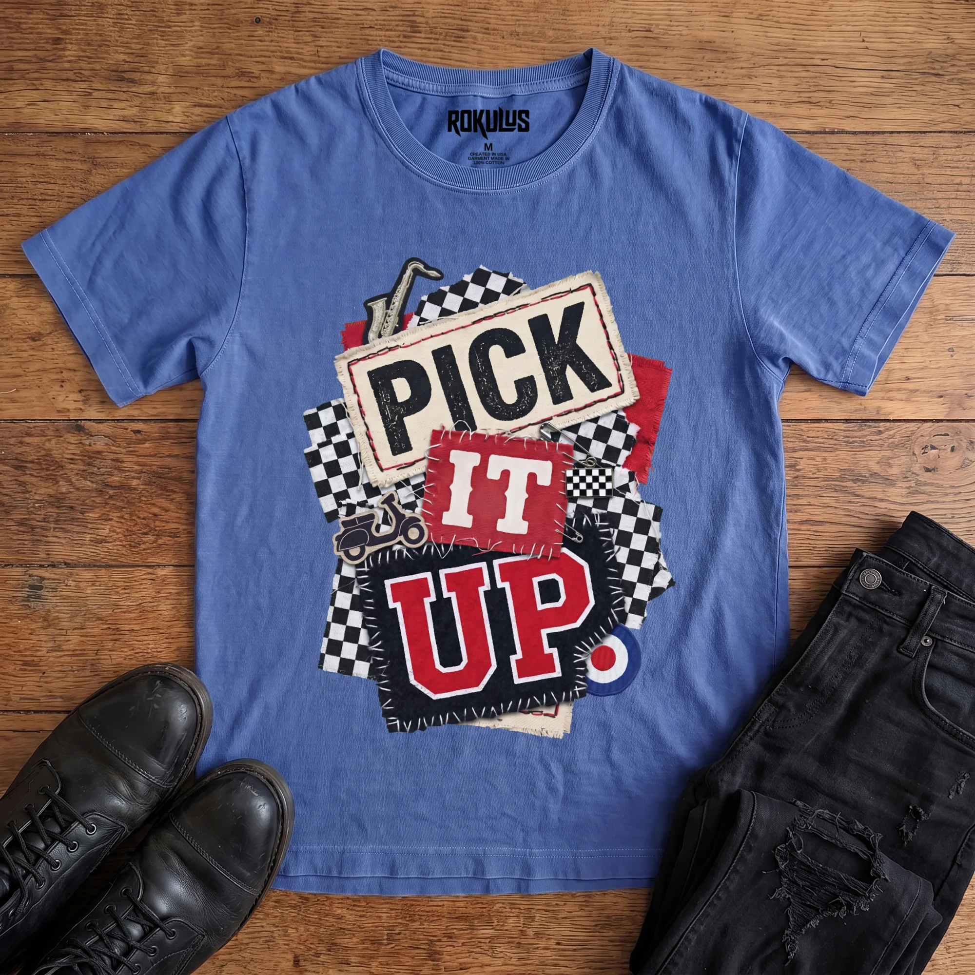Washed royal blue Rokulus Pick It Up Ska vintage graphic tee laid flat on wood with black boots and jeans, front print showing a 2-tone ska collage with checkerboard, saxophone, scooter, and mod target under stitched "Pick It Up" lettering