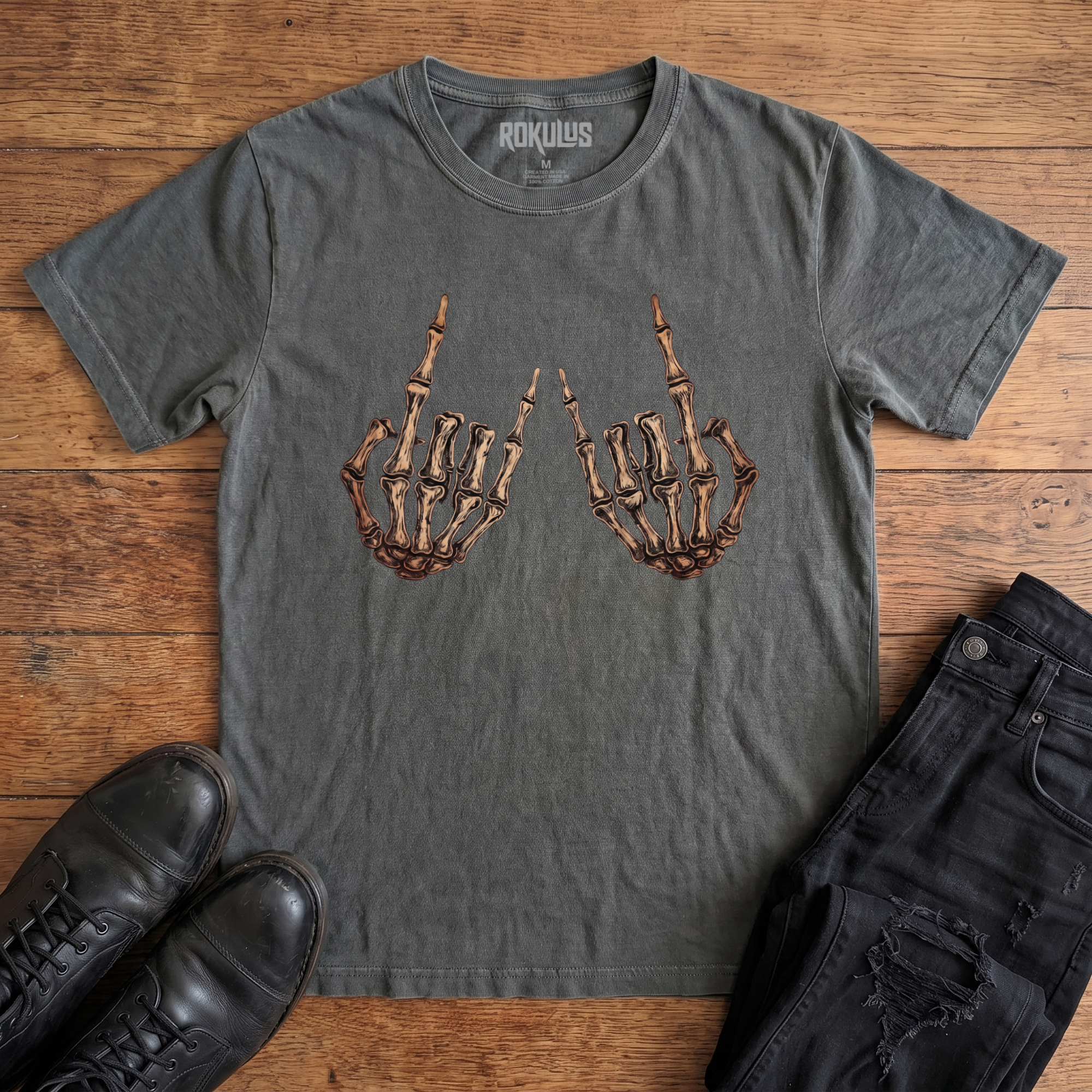 Washed charcoal Rokulus Skeleton Rocker Hands vintage graphic tee laid flat on wood with black boots and jeans, front print showing two skeletal hands thrown up in the rock and roll horns sign in detailed bone and cream tones