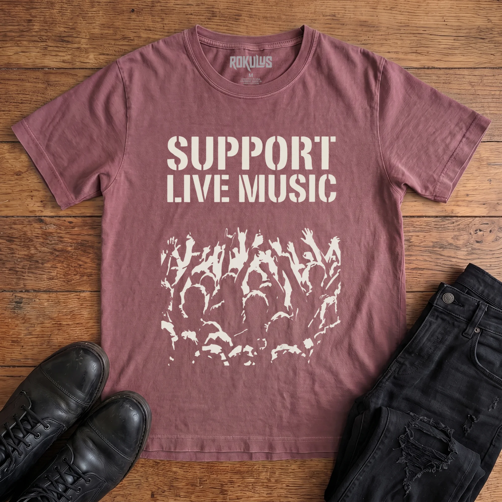 Washed maroon Rokulus Support Live Music vintage graphic tee laid flat on wood with black boots and jeans, front print showing "Support Live Music" in stencil type above a silhouetted concert crowd with raised hands