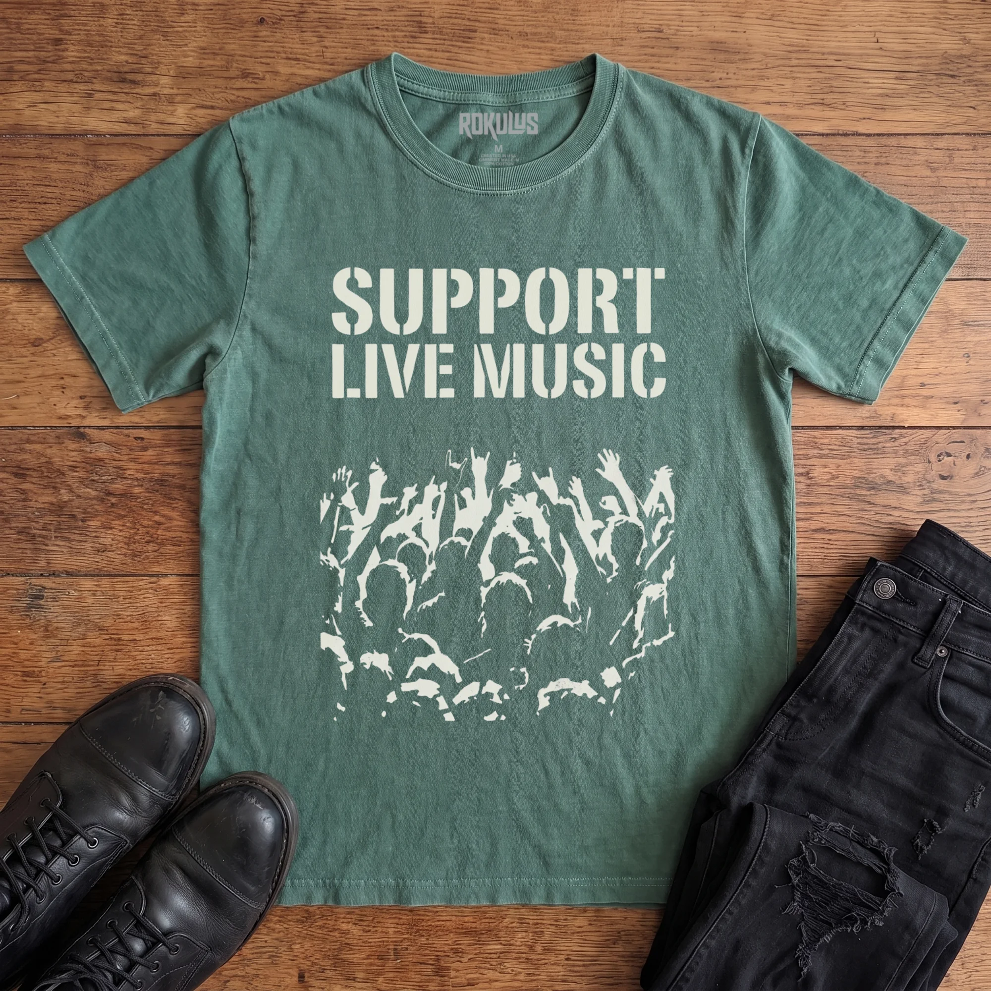 Washed pine Rokulus Support Live Music vintage graphic tee laid flat on wood with black boots and jeans, front print showing "Support Live Music" in stencil type above a silhouetted concert crowd with raised hands